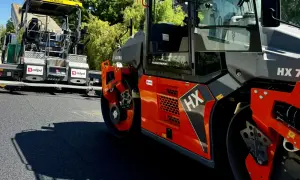 Asfaltowóz i walec drogowy w akcji, przygotowujące nawierzchnię.